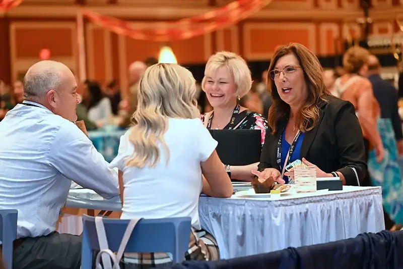 A group of four people engaged in conversation at a table in a busy event setting.