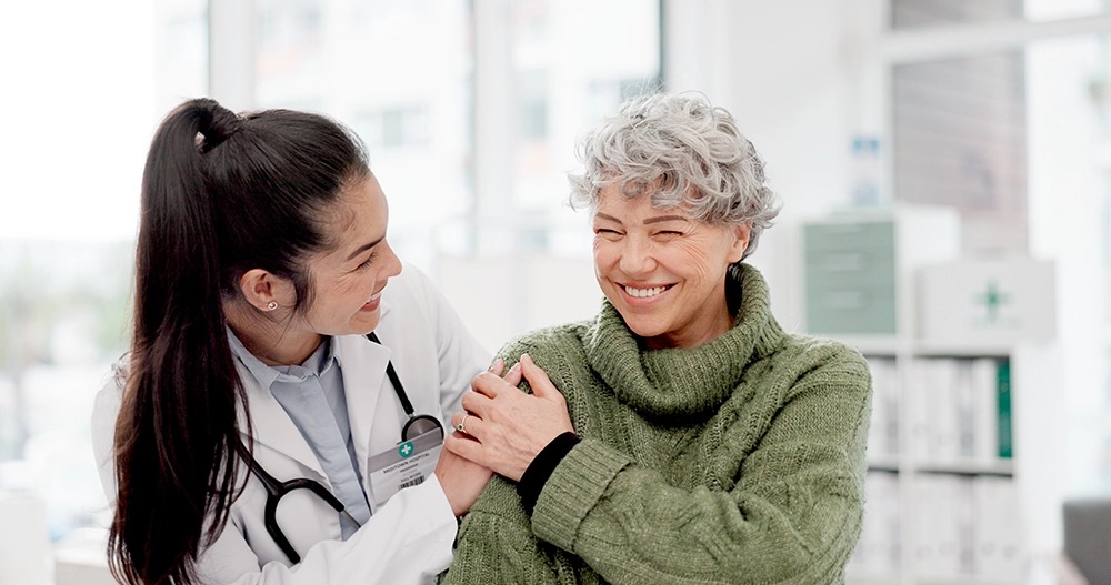 A smiling doctor and an elderly woman share a joyful moment in a bright, modern medical office.