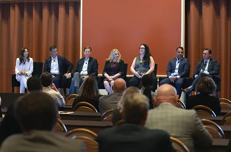 A panel discussion featuring seven speakers on stage, with an audience visible in the foreground.