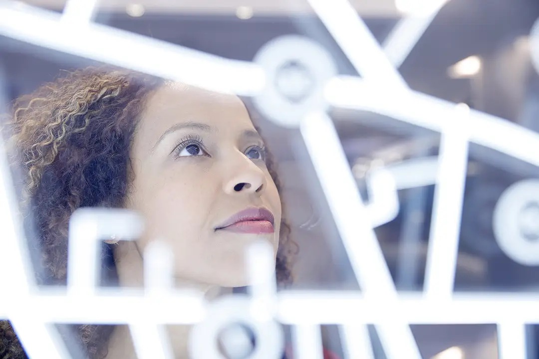 A woman gazes thoughtfully at a glass display with abstract designs, showcasing her curiosity and contemplation.