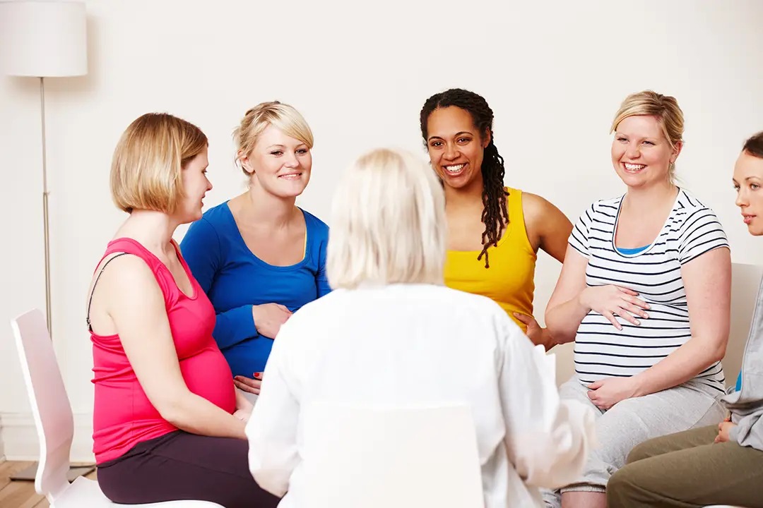 A group of pregnant women sitting in a circle, engaged in conversation with a facilitator.